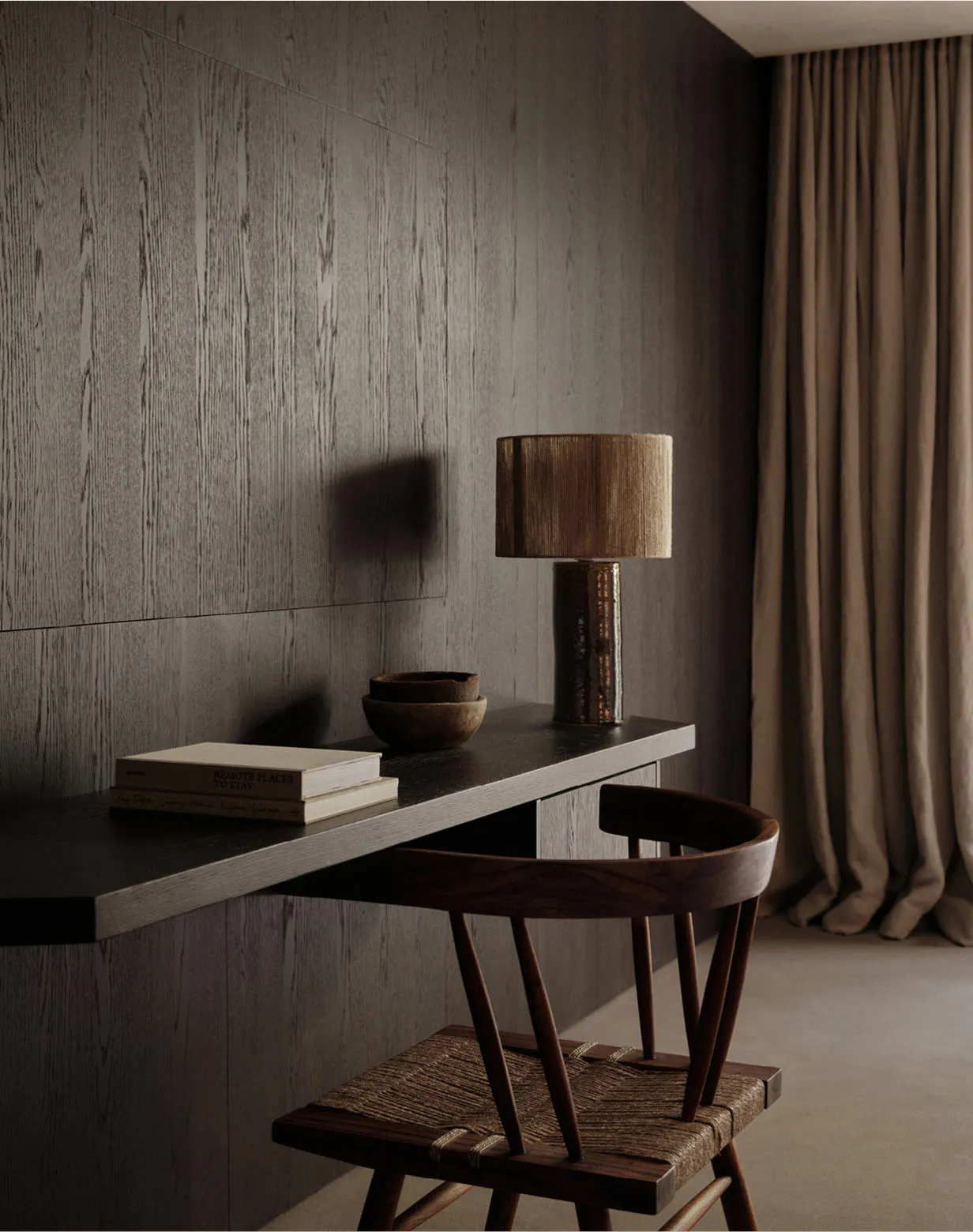 A modern home office desk with a wooden chair, lamp, and a few books.