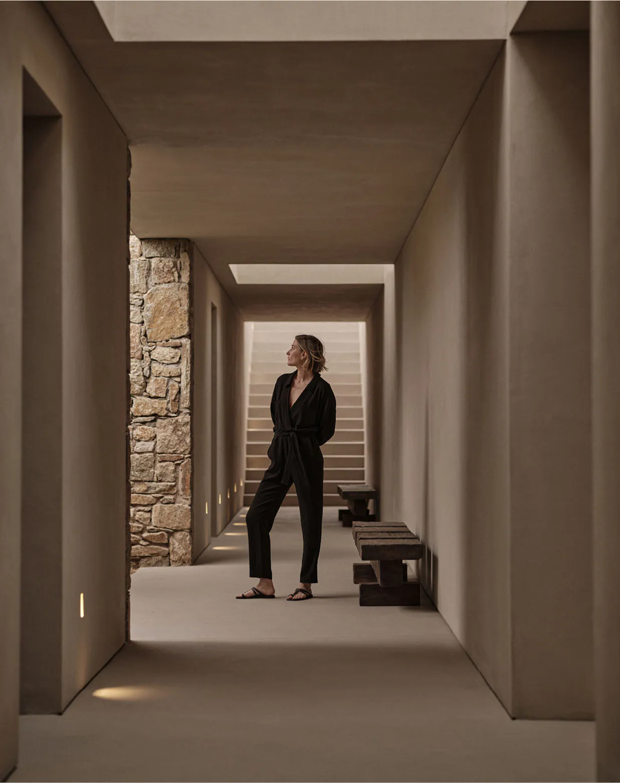 A person standing in a modern interior hallway with concrete walls and stone accents.