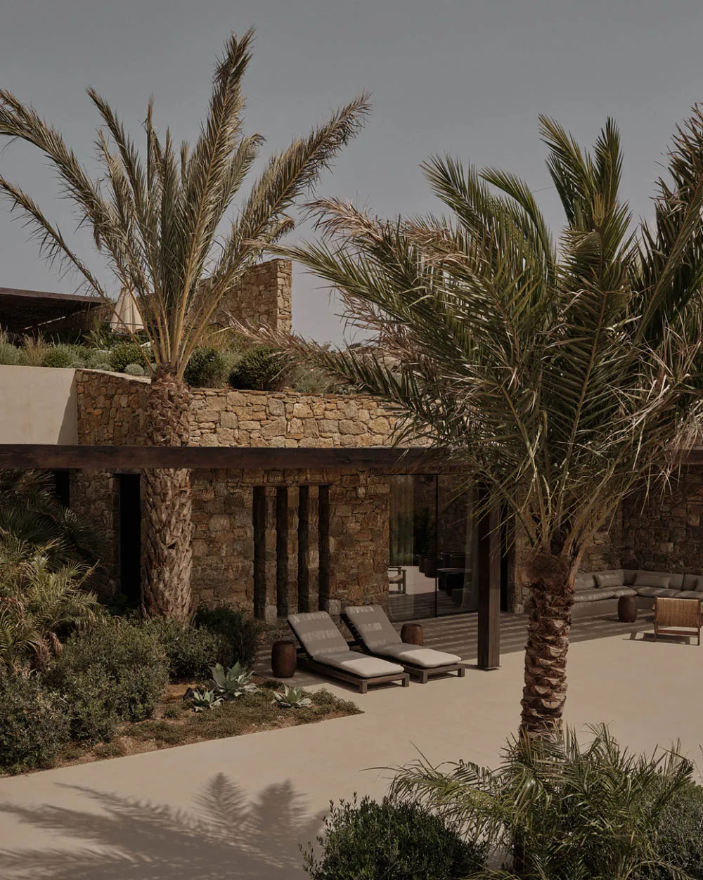 Modern residential exterior featuring a poolside lounge area with stone and concrete materials, decorated with palm trees.