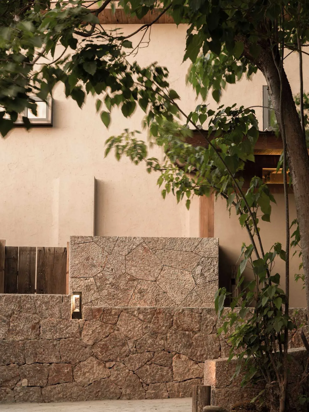 Modern residential exterior featuring a stone-clad wall and surrounding greenery.