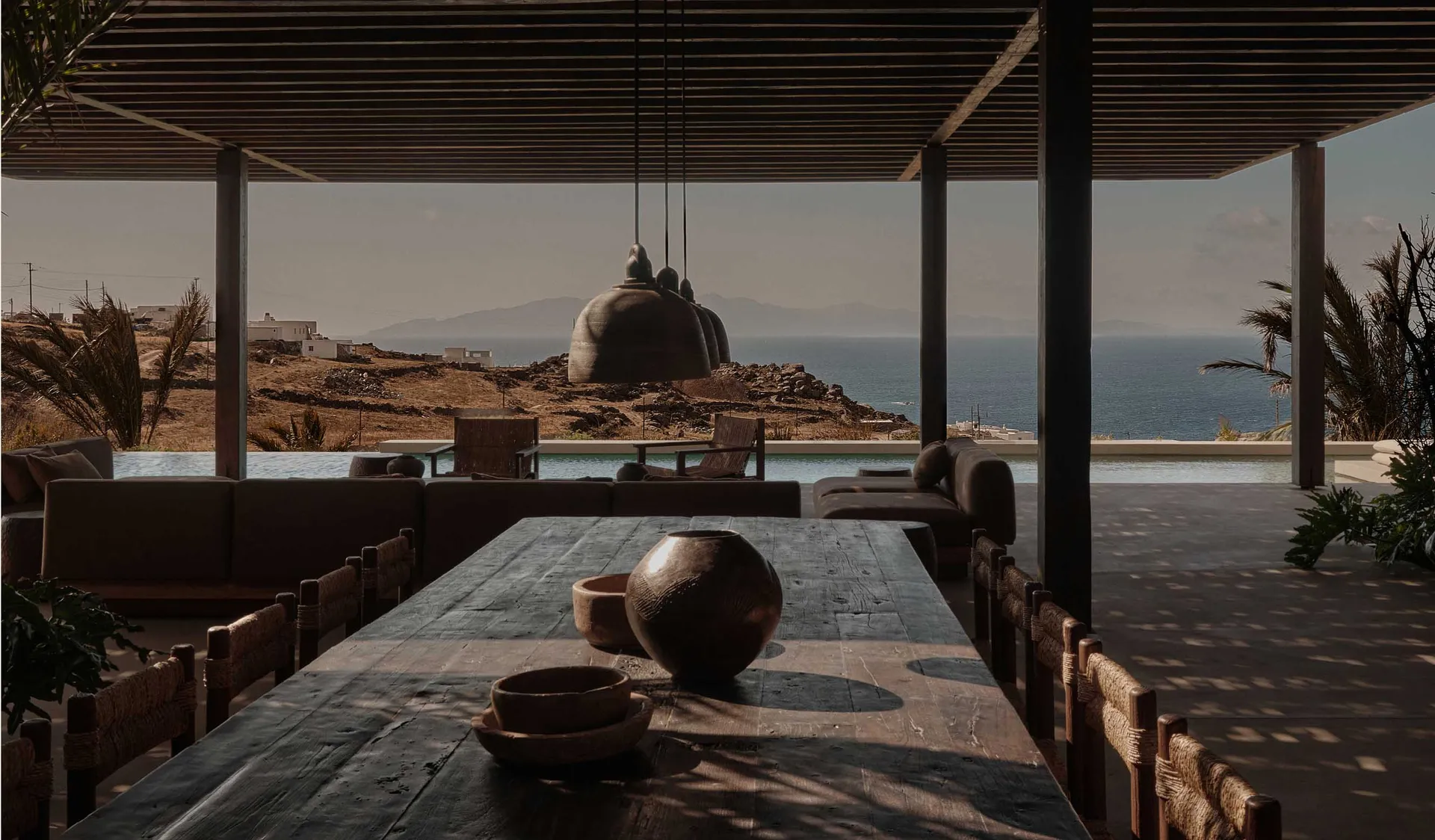Minimalist outdoor living space with concrete and wooden materials, featuring a dining area, seating, and a pool with a view