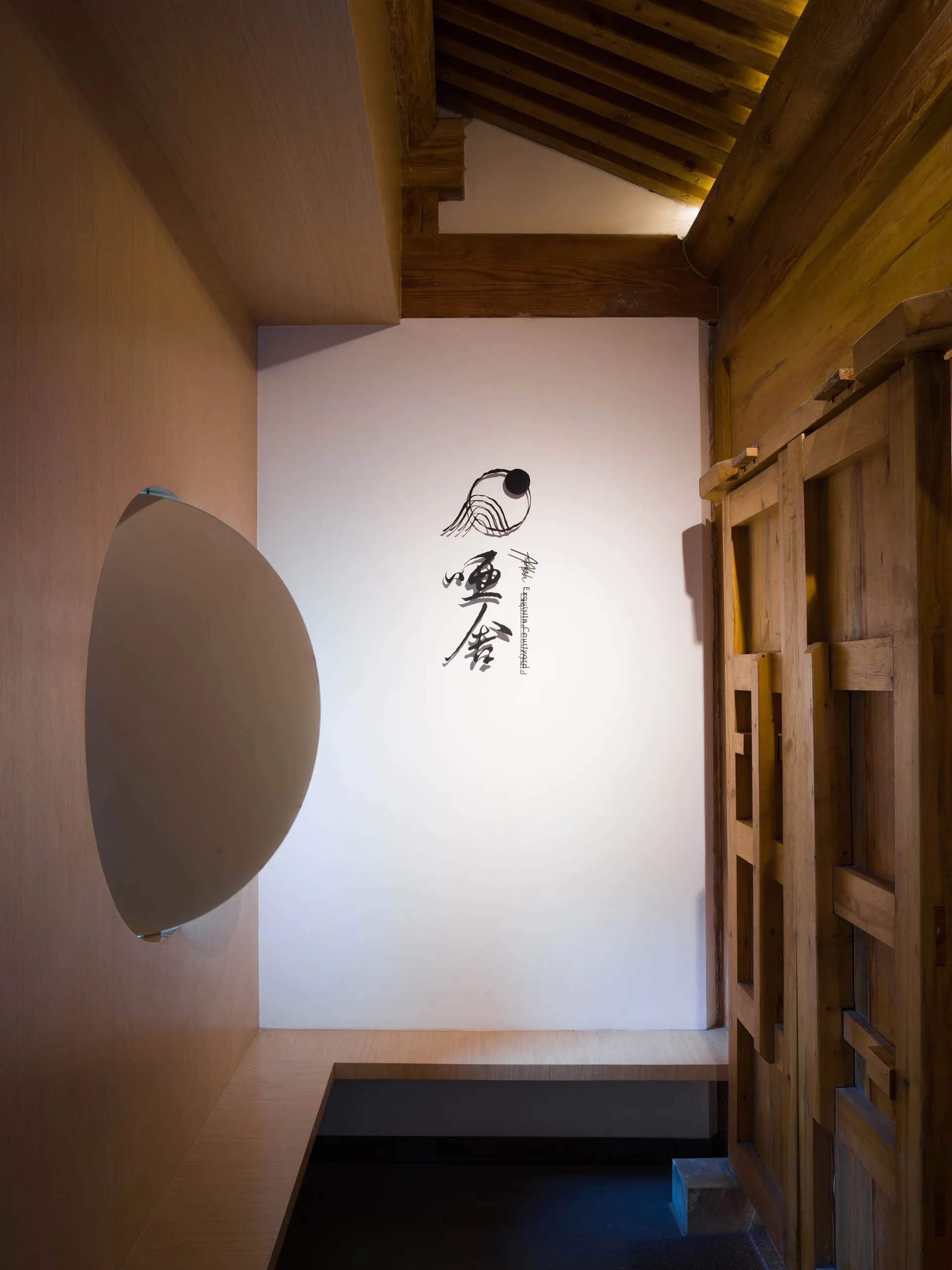 A minimalist wooden interior with a white circular light fixture and traditional Japanese calligraphy on the wall.