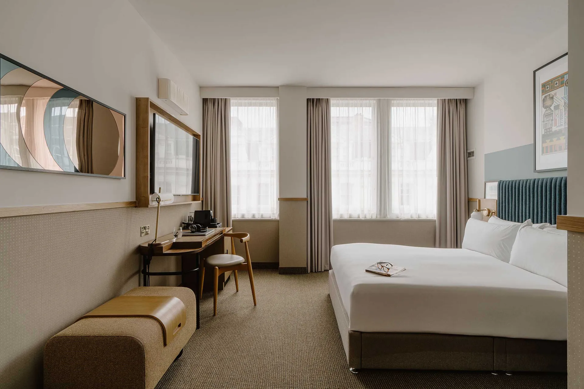 A modern hotel room with a king-sized bed, a work desk, and a large window.