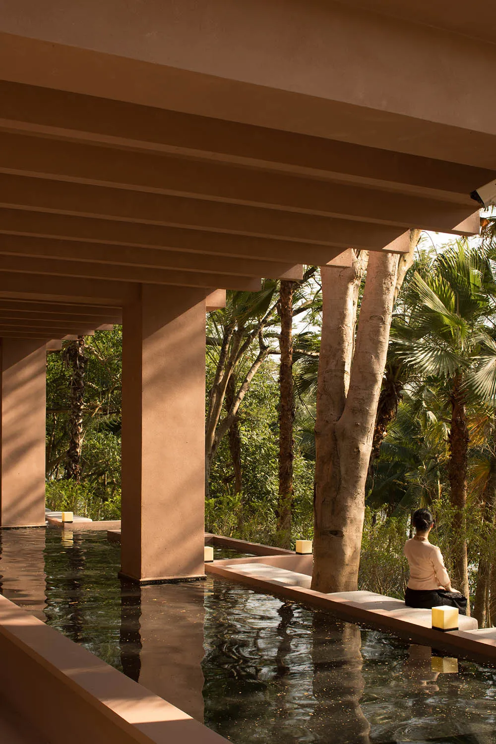 A modern outdoor space with concrete elements, a water feature, and a person relaxing on a bench.