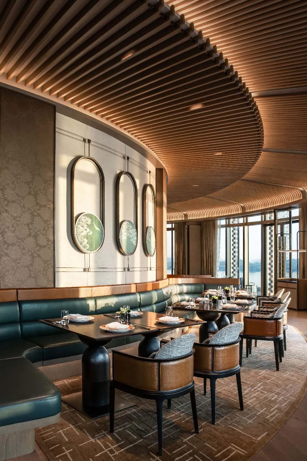 Luxurious restaurant interior with wooden slat ceiling, green banquettes, and wooden tables.