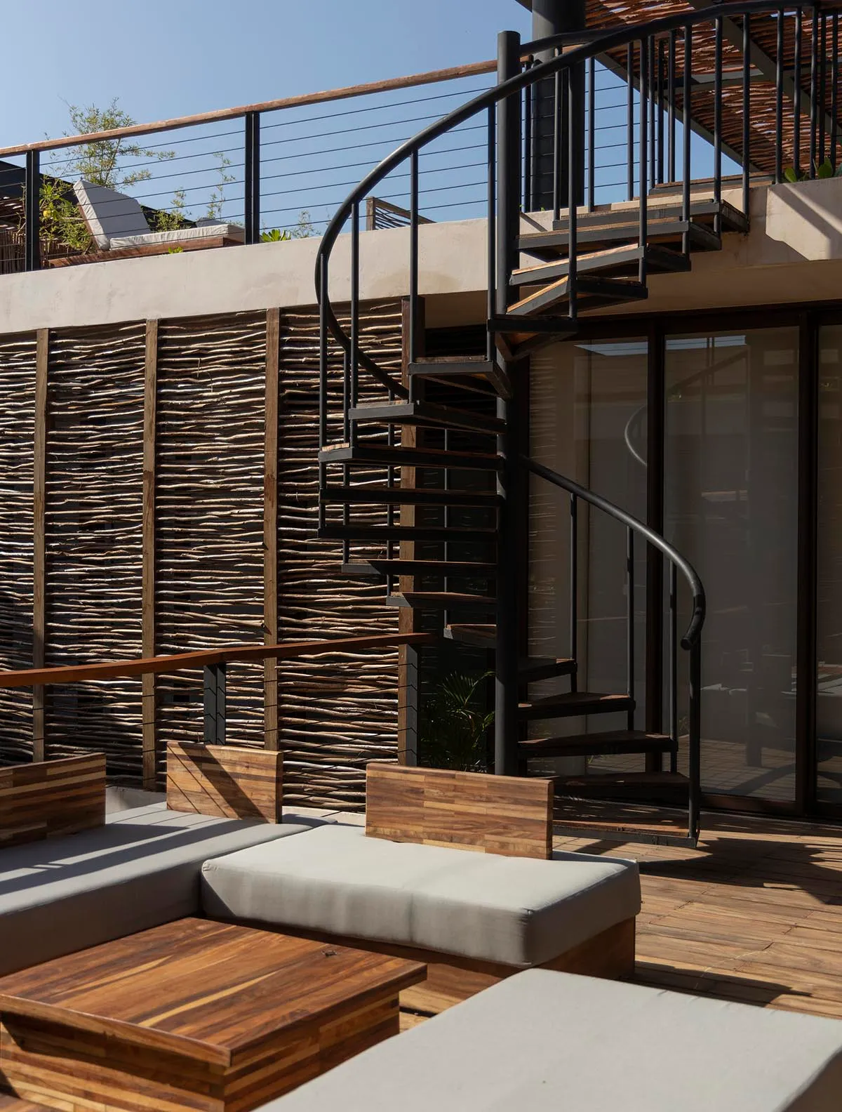 An industrial-style balcony featuring black metal stairs, wooden seating, and a wicker wall