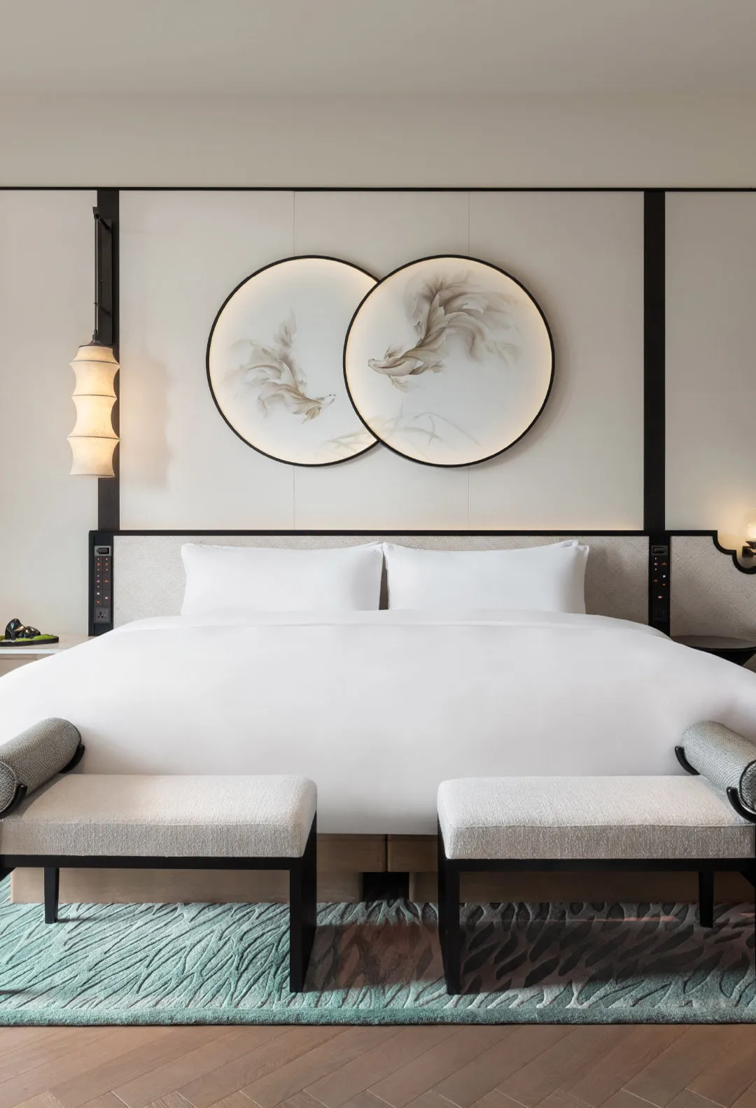 A minimalist bedroom featuring a bed with white textiles, mounted artworks on the wall, and a wooden floor with metal accents