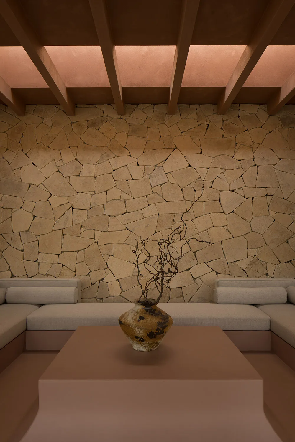 A minimalist living room with a stone wall and beige seating.