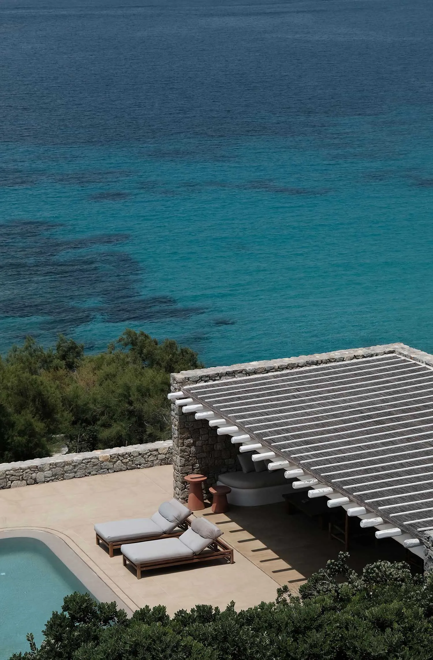 Two lounge chairs and a sunbed by a pool with a stone/concrete roof.