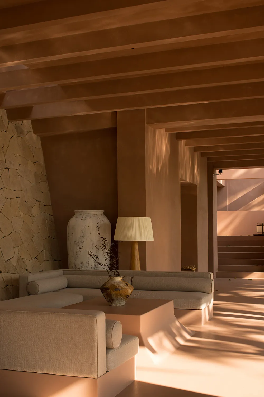 A minimalist, modern living room featuring a concrete floor and walls, with a sleek sofa, lamp, and decorative vase.