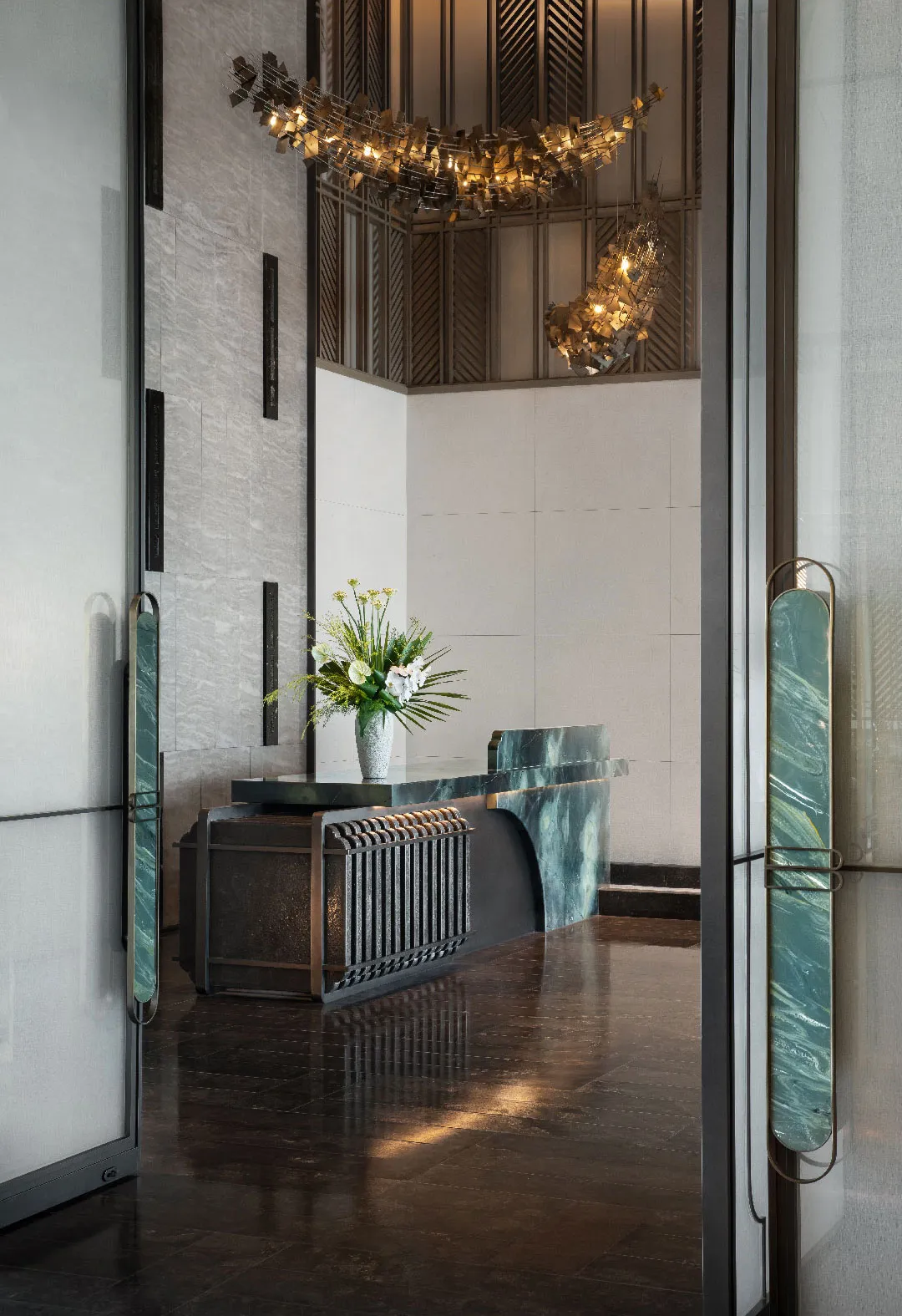 Modern lobby reception with marble counter, concrete texture, brass accents, and floral arrangement.