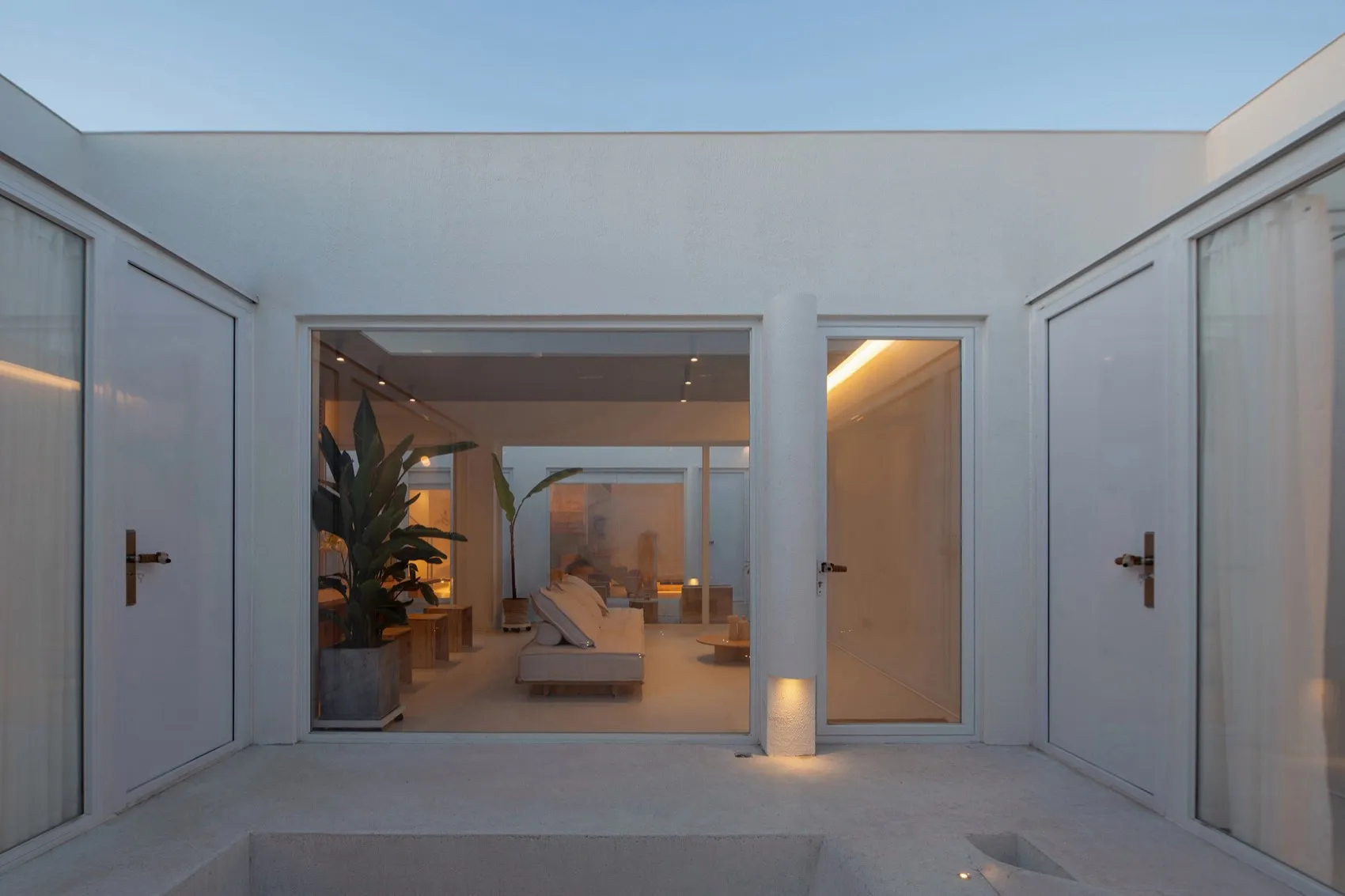A minimalist living room with concrete walls and floor, featuring a white sofa and illuminated by warm lighting from the ceil