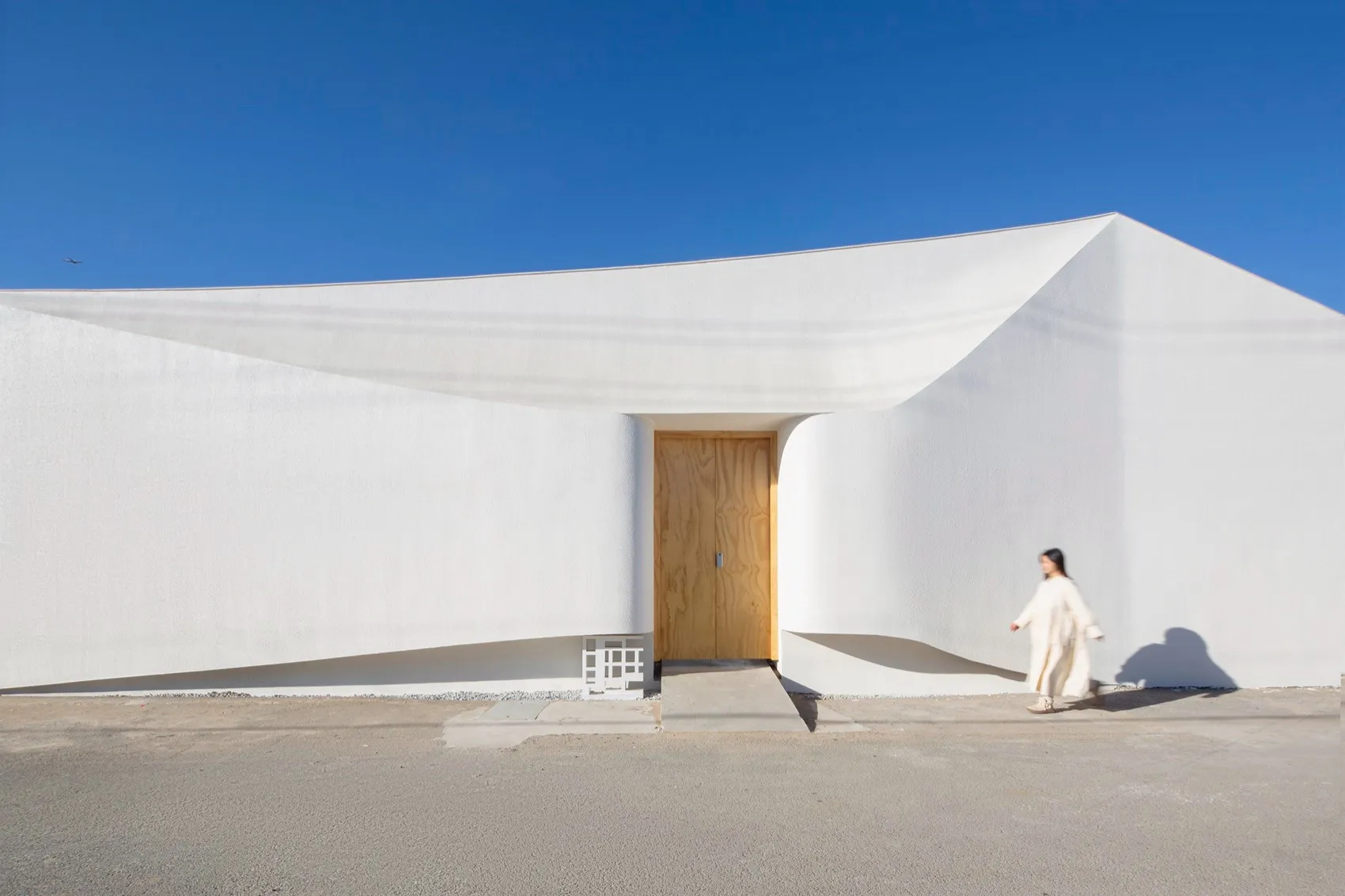 A minimalist white building with a concrete facade and a wooden door.
