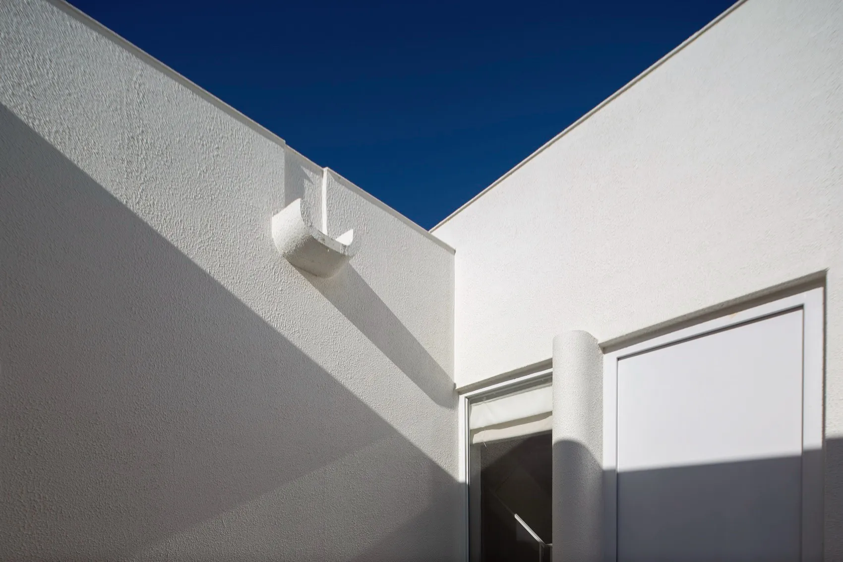A white modern house with a corner view showing the facade and roof.