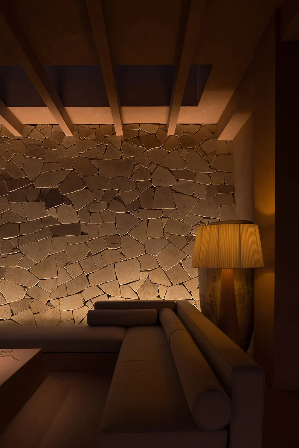A modern interior space featuring a stone wall and a cozy seating area with a lit lamp, designed to provide comfort and style