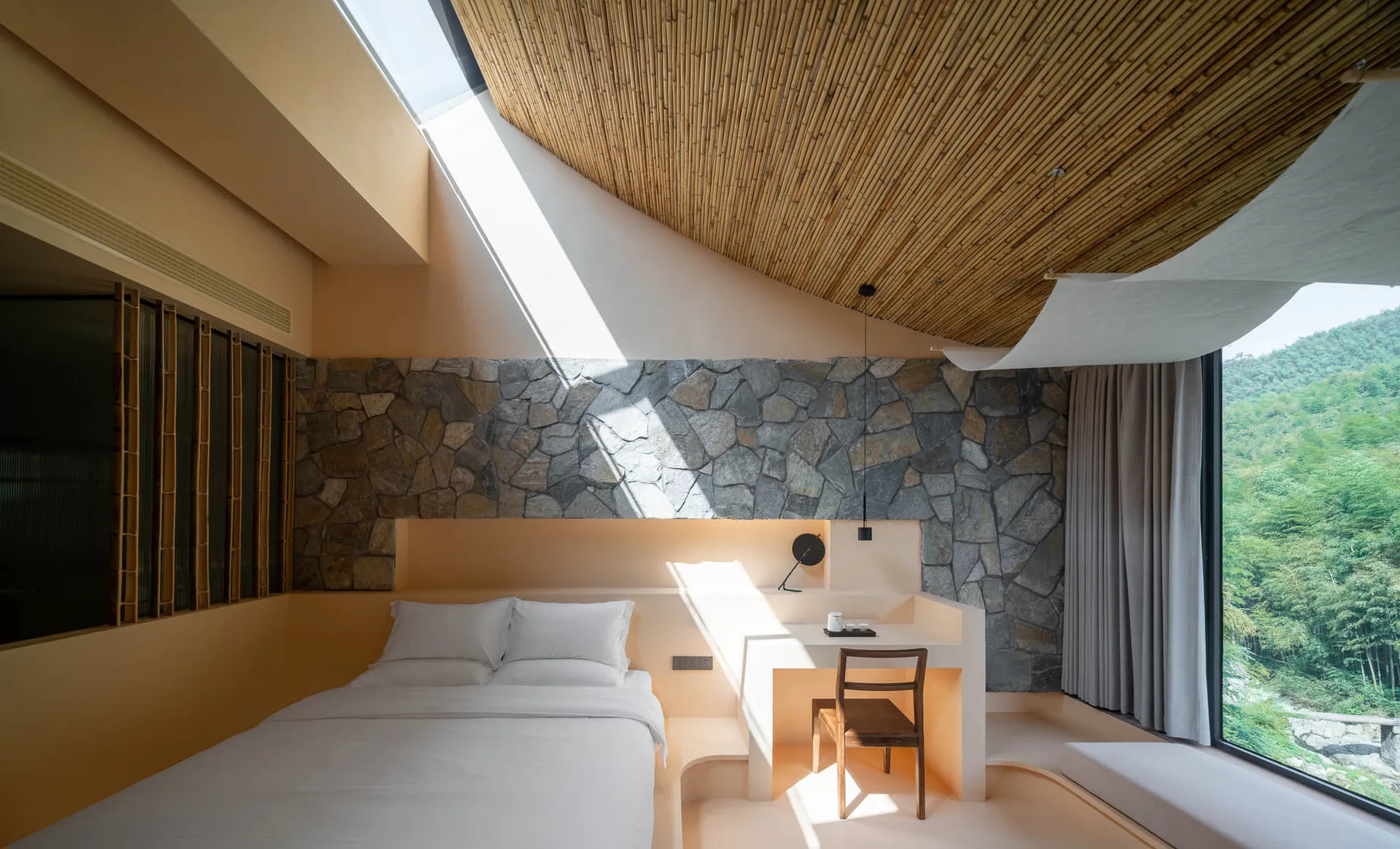 A serene, minimalist bedroom with concrete walls, a skylight, and a view of the mountains.