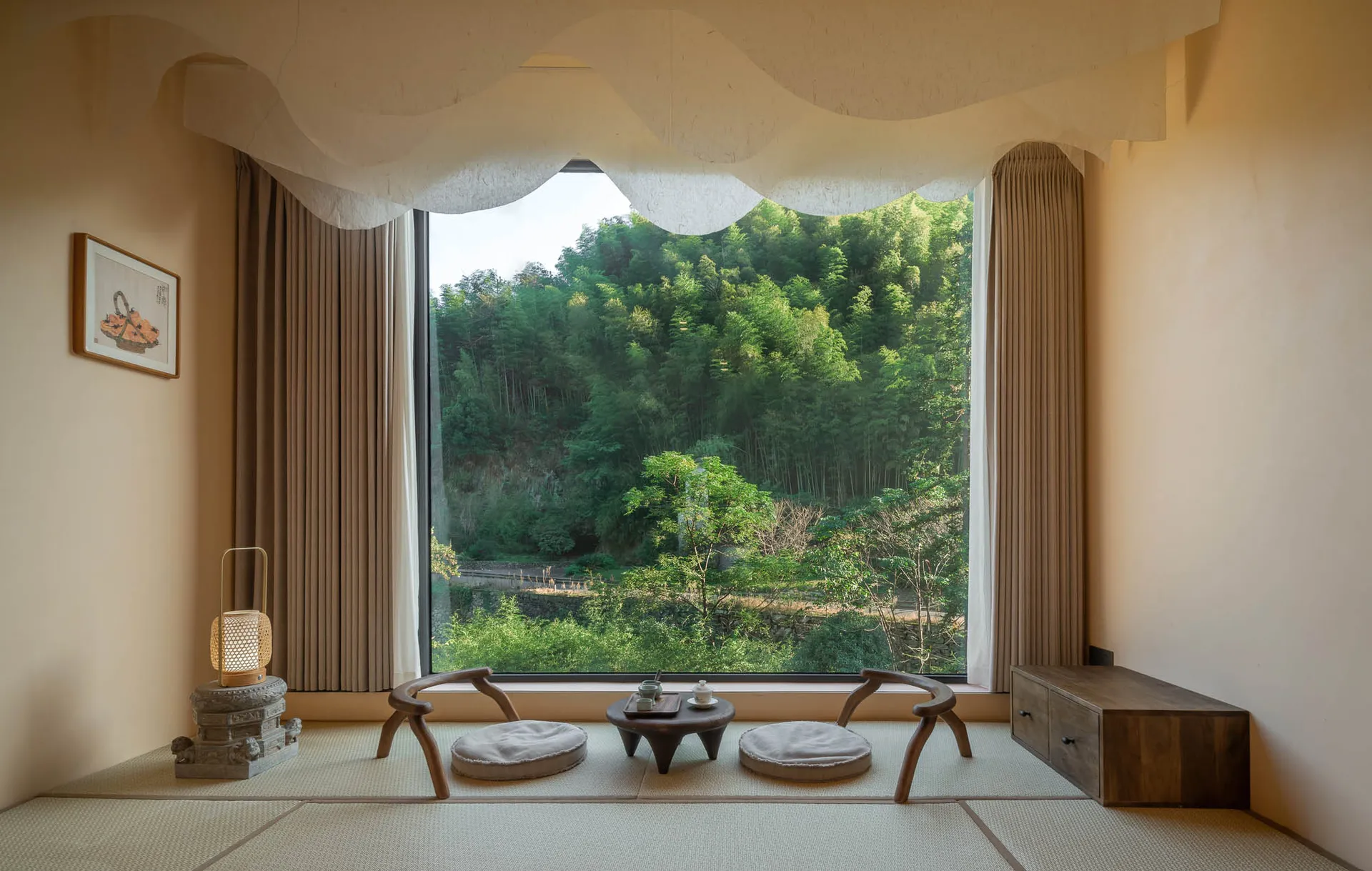 A minimalist living room with natural materials, featuring two cushions, a small wooden table, and a large window overlooking