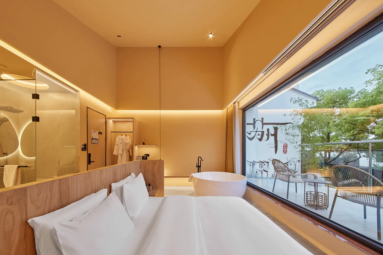 Minimalist bedroom with white furniture and a large window overlooking a garden.