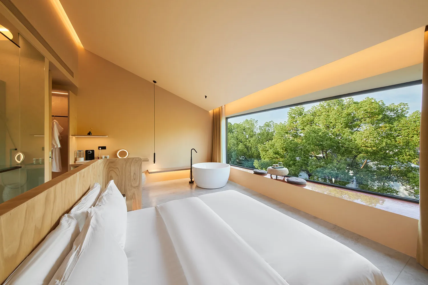 Modern minimalist bedroom with white bedding, wooden headboard, and large window overlooking green trees.