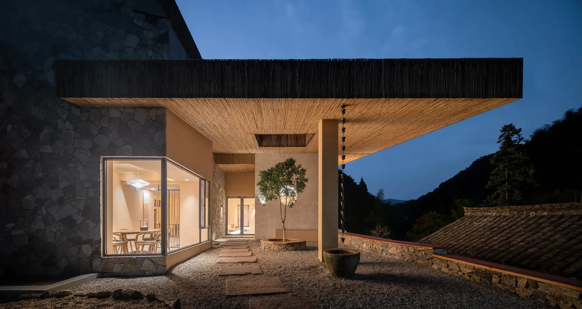 A modern residential building with stone, concrete, and wooden materials outdoors at dusk.