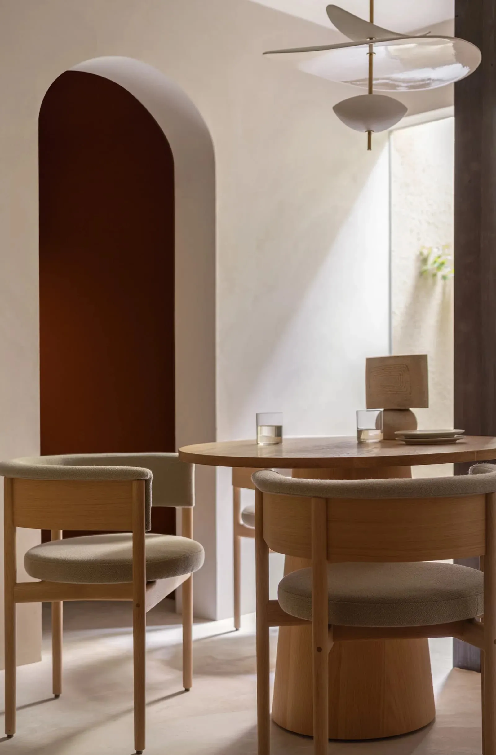 A minimalist dining room with wood furniture and light-colored cushions.