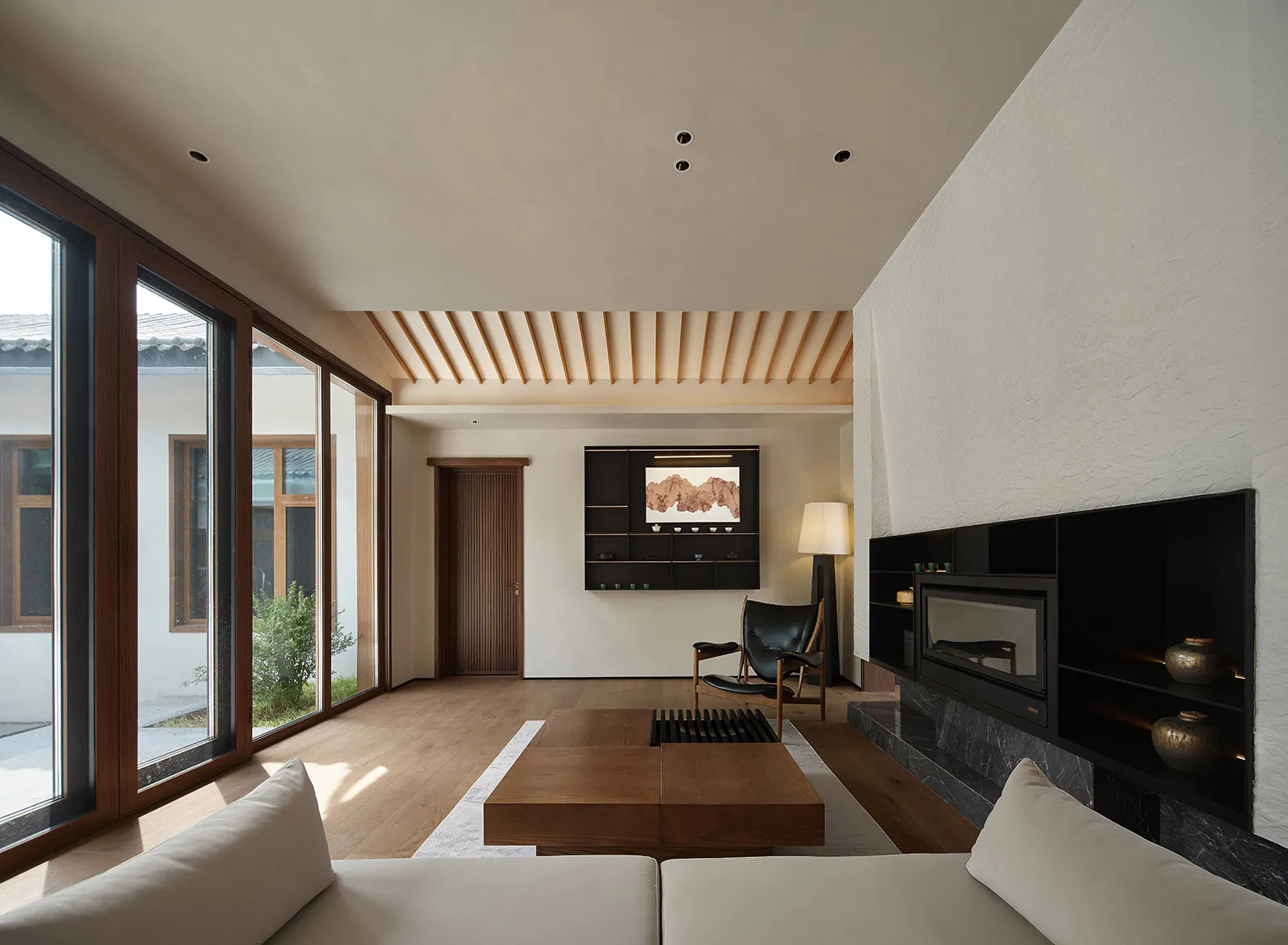 Modern minimalist living room with wooden furniture, floor-to-ceiling windows, and a cozy fireplace
