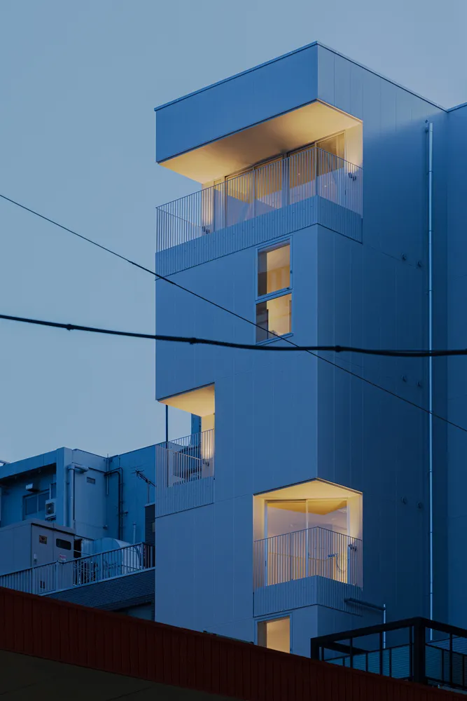 Square, modern apartment building with blue hues featuring illuminated windows and balconies.