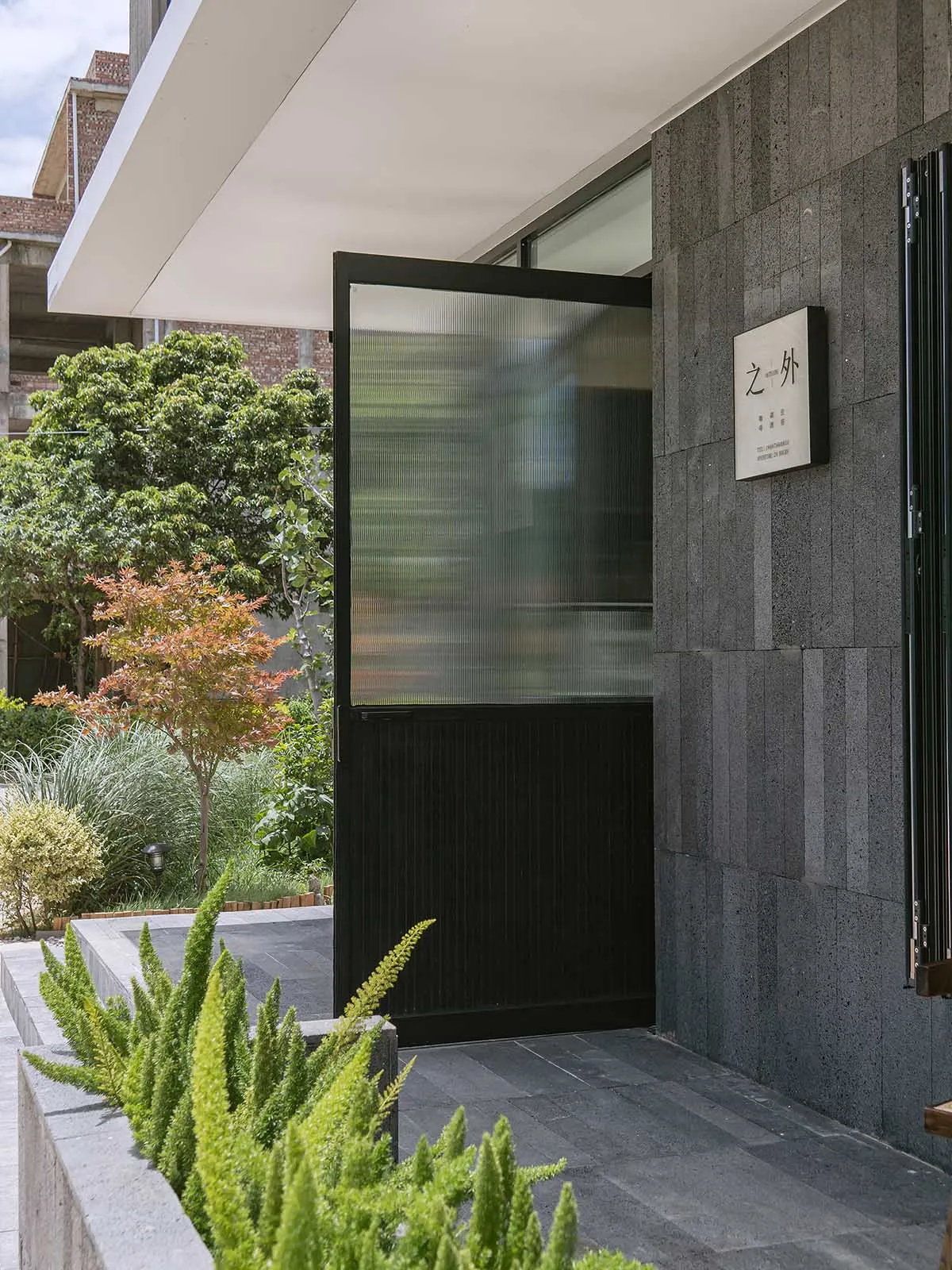 A modern building exterior featuring a black door with glass panels and a concrete facade.