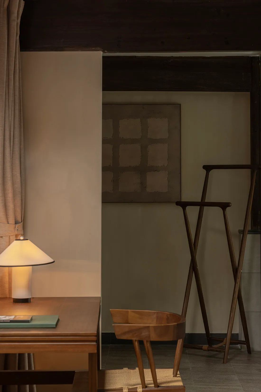 A modern minimalist living room featuring a wooden chair, a simple table lamp, and a minimalist artwork.