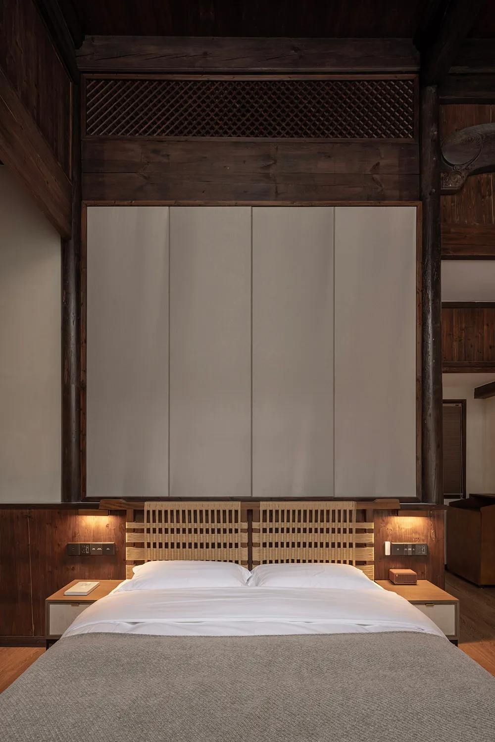 Modern minimalist bedroom featuring a wooden frame and woven headboard with white furniture, designed for relaxation and simp
