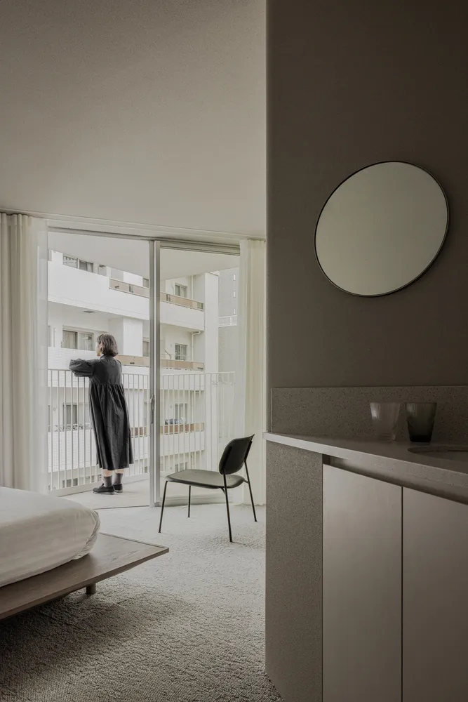 A modern grey bedroom with a circle mirror, wooden bed, and white curtains.