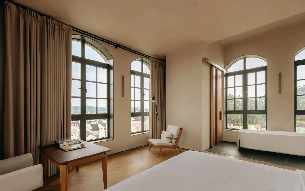 Modern minimalist bedroom with a white bed, wooden floor, and large windows.