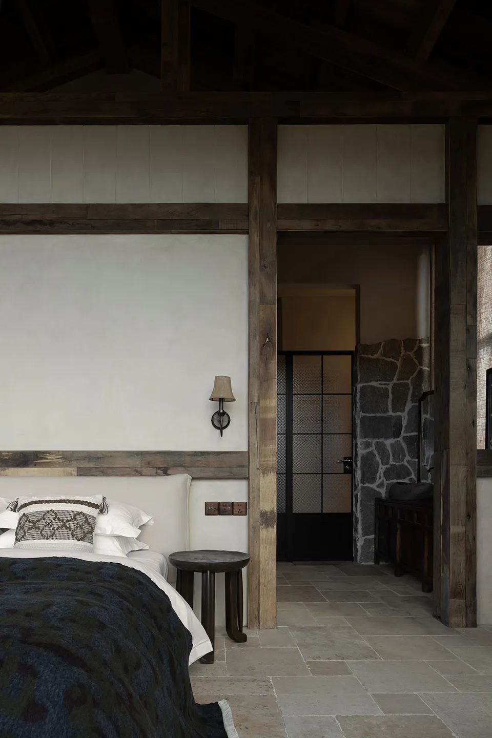Minimalist bedroom with white walls, wooden accents, and a bed with a blue and black patterned blanket.