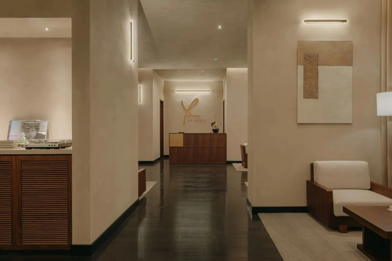 Modern, minimalist hotel reception area with sleek, dark wood flooring, beige seating, and a sleek reception desk with the ho