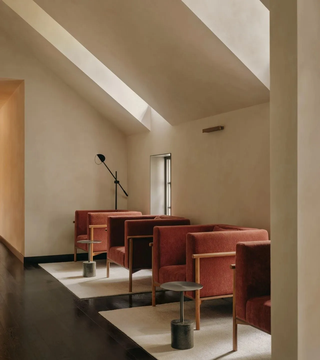 A minimalist living room with red fabric sofas, wooden tables, and concrete floor.