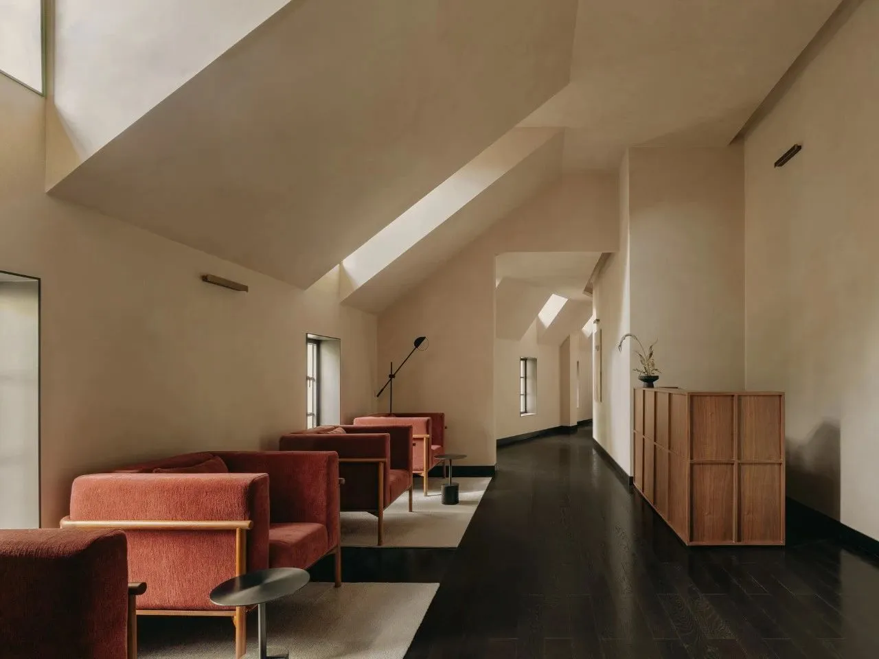 A modern living room with red upholstered furniture, dark hardwood floors, and white walls.