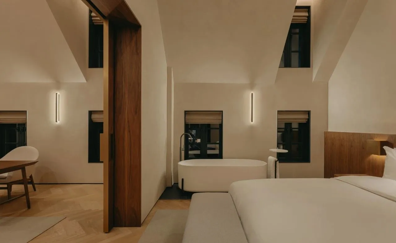 Modern minimalist bedroom featuring a white bed, white bathtub, and beige walls with plaster finish.