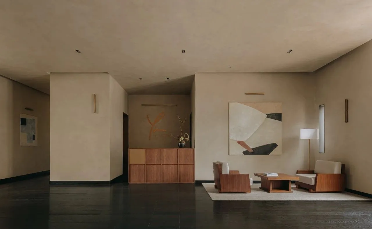 A minimalist lobby featuring concrete walls, wooden furniture, and fabric seating.