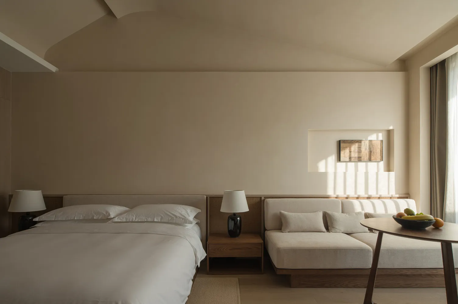 A serene minimalist bedroom with a bed, couch, and a fruit bowl on a table.