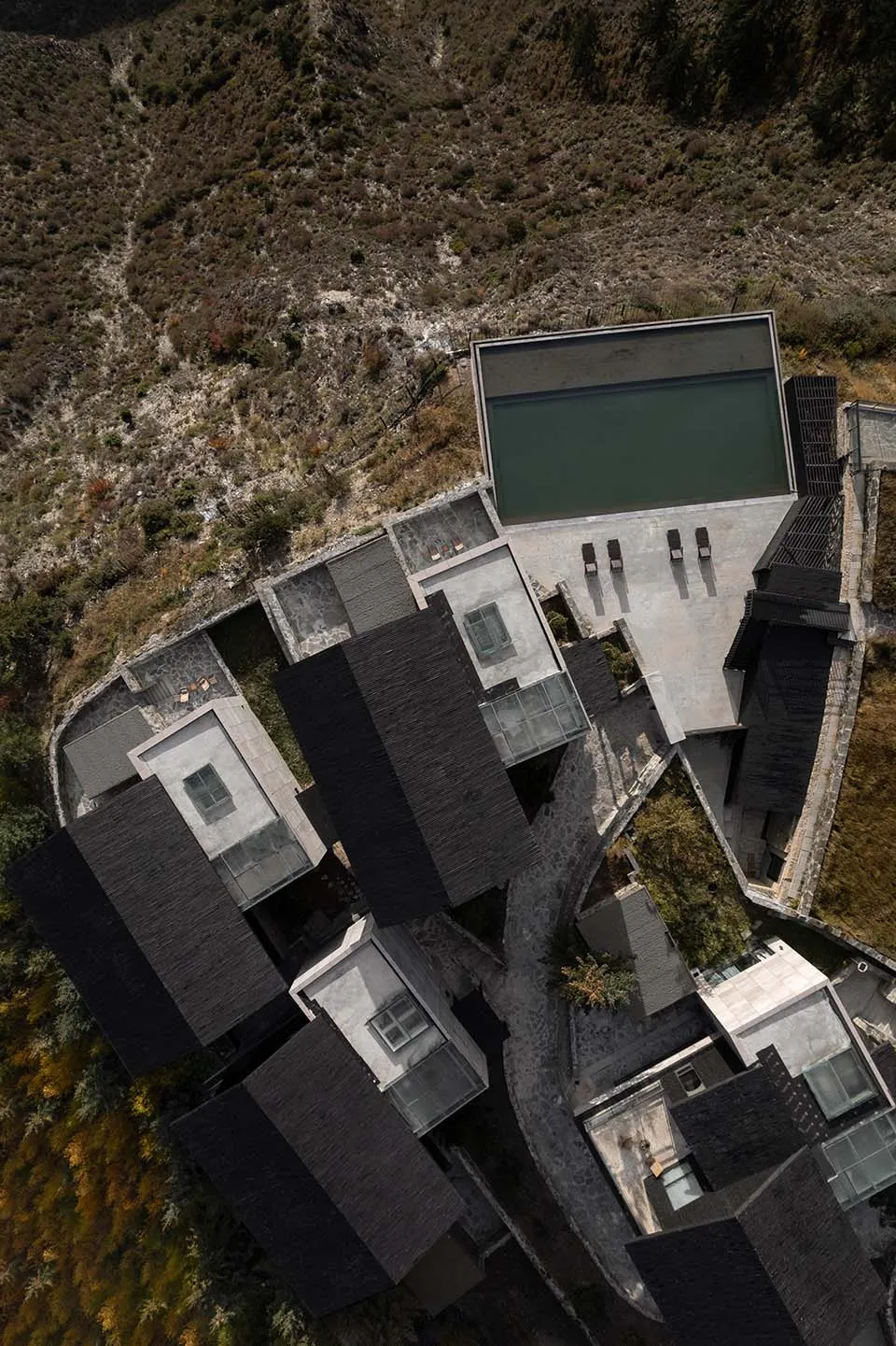 Aerial view of a modern pool house featuring concrete, glass, and stone materials.