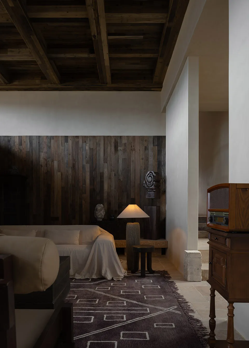 A modern minimalist living room with white furniture, wooden ceiling beams, and a marble floor, featuring a floor lamp and a