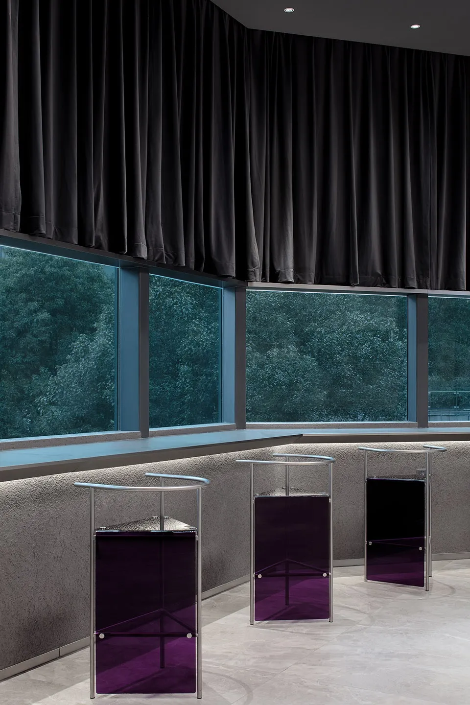 Modern hotel lobby with glass and metal furniture and black curtains.