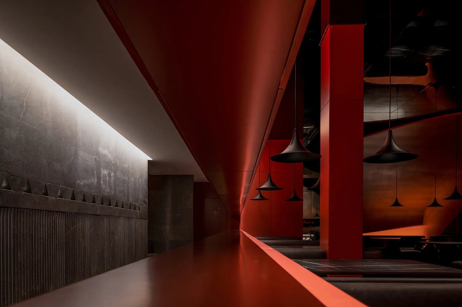 A sleek, modern food court with red metallic walls and pendant lights hanging from the ceiling.