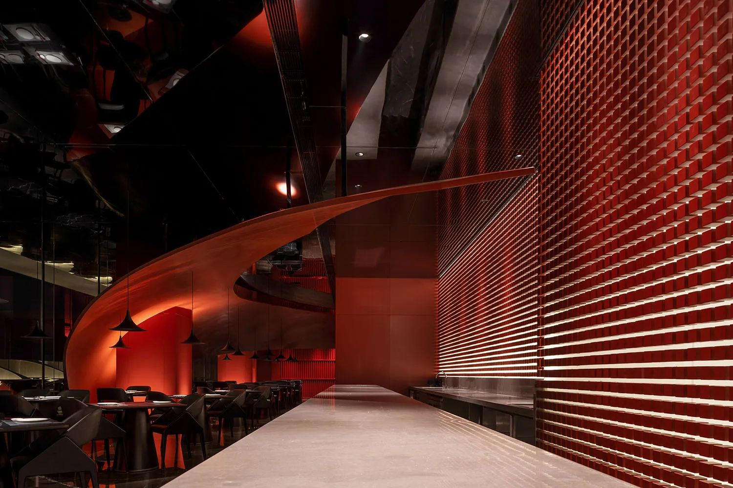 A modern restaurant interior with a red metallic tile wall and sleek bar counter.