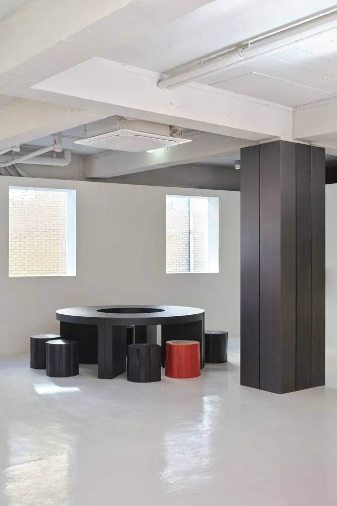 A modern industrial conference room featuring a black circular table, red stool, and concrete space.