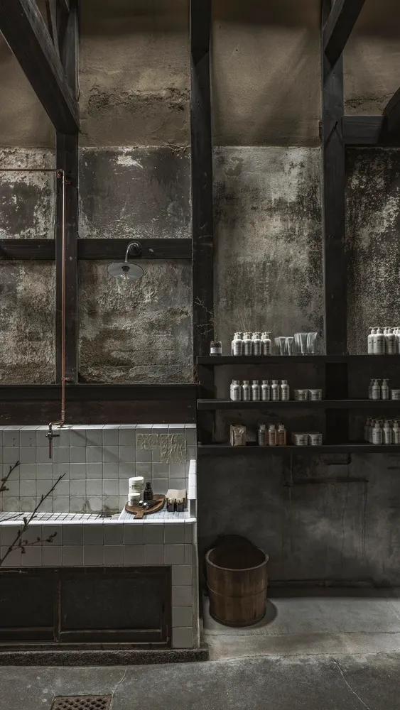 A modern, industrial-style bathroom with concrete walls and exposed beams, featuring a shower head mounted on the wall and va