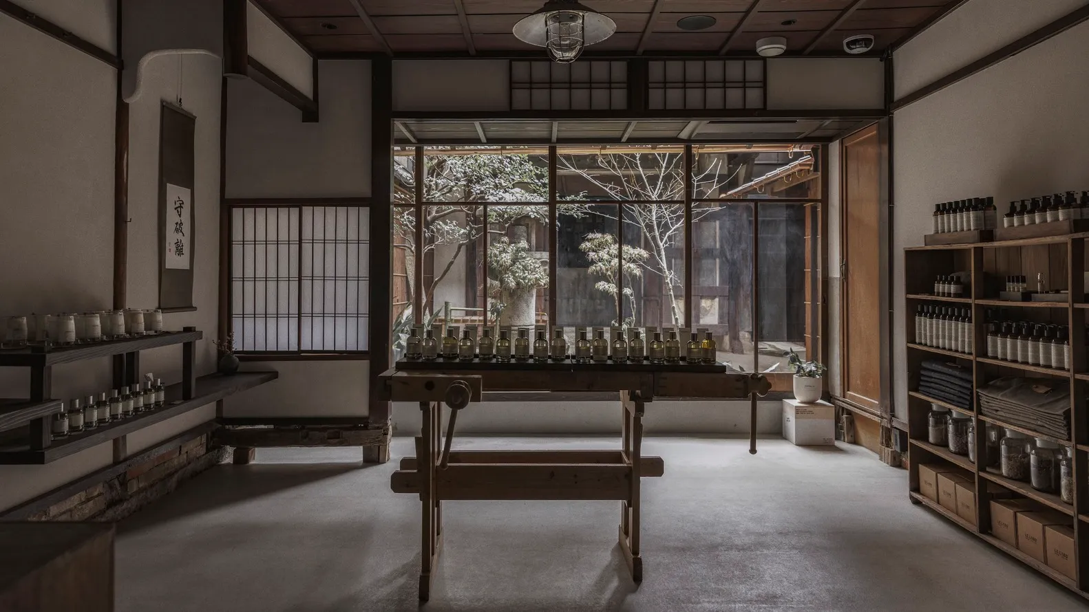 A traditional retail storefront with a wooden bench and bottles lined up on a table, viewed through a window with white paper
