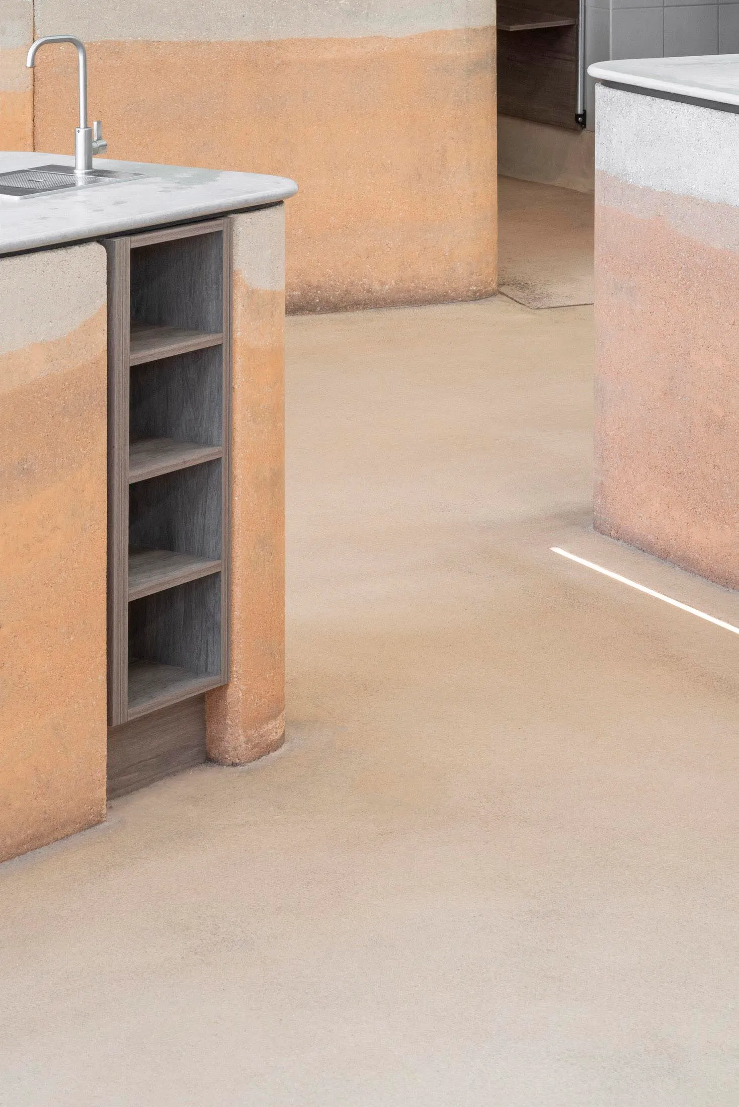 Modern minimalist kitchen featuring exposed concrete walls and flooring with a built-in wooden shelving unit.