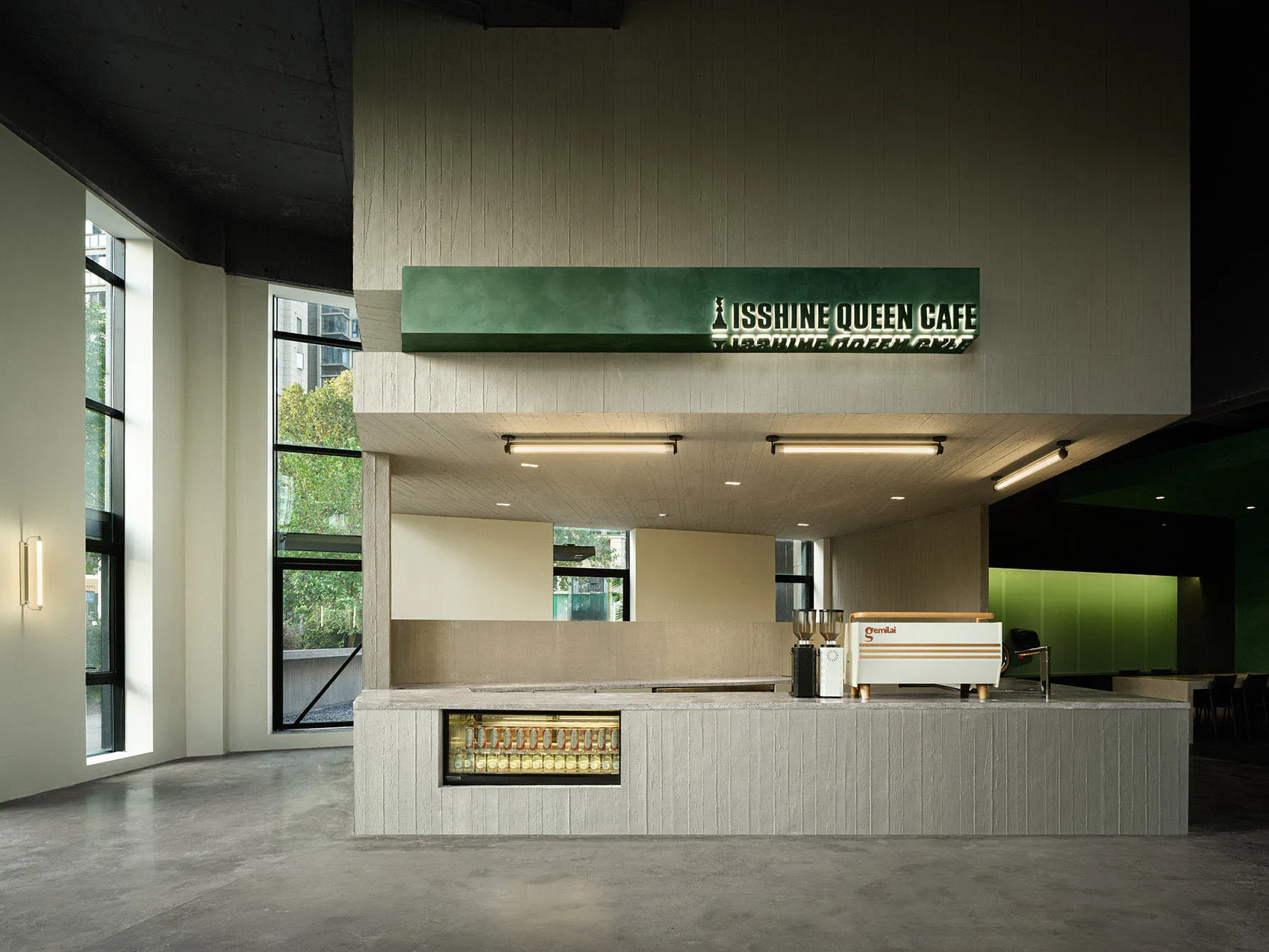 A minimalist cafe interior with a green concrete bar, featuring a sign with the name Isshine Queen Cafe.