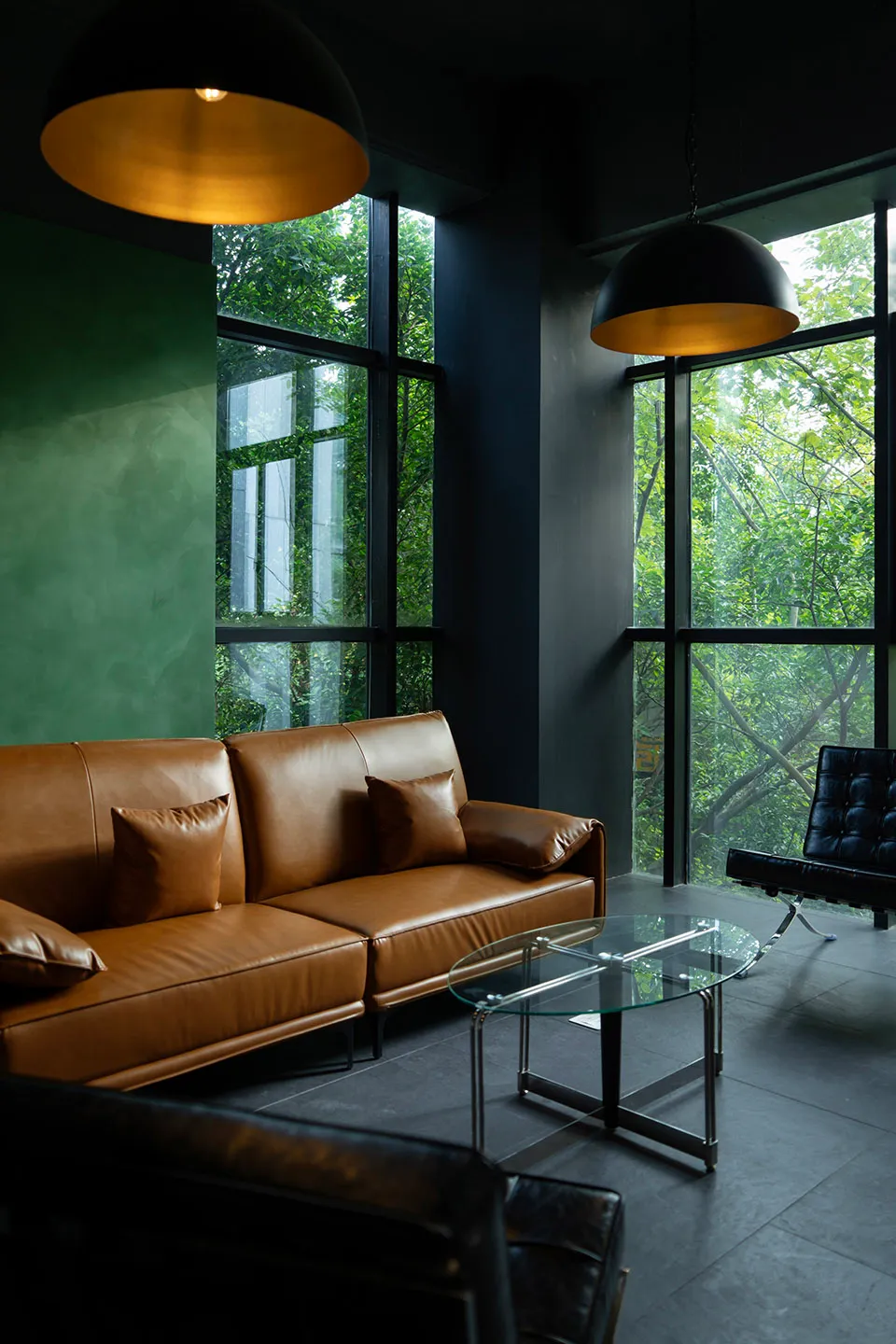 A modern living room featuring a brown leather sofa with glass coffee table and concrete walls.